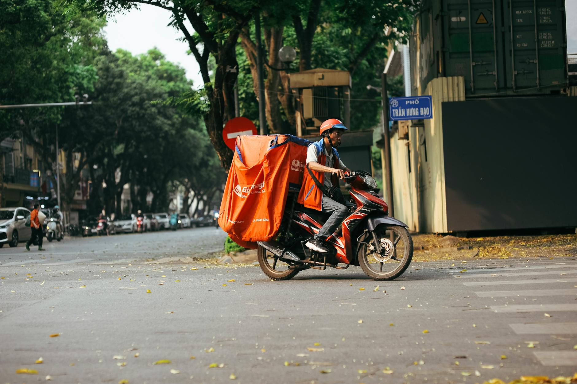 A delivery driver transports goods on a motorcycle in a bustling city street scene.