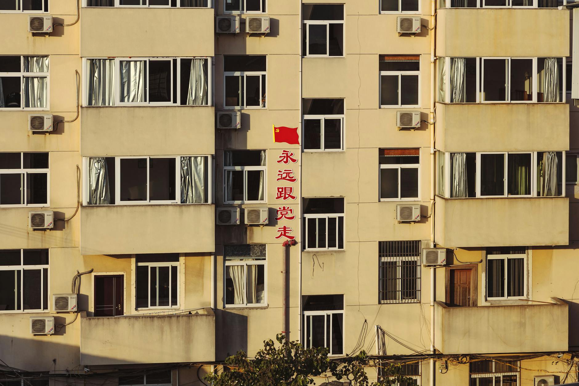 Facade of high building with red Chinese inscription in residential area in light of sun